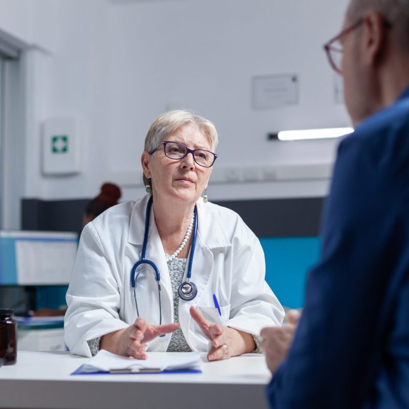 Doctor and patient meeting at consultation appointment to do healthcare checkup in cabinet. Medic talking to aged man about diagnosis and treatment after examination at medical visit