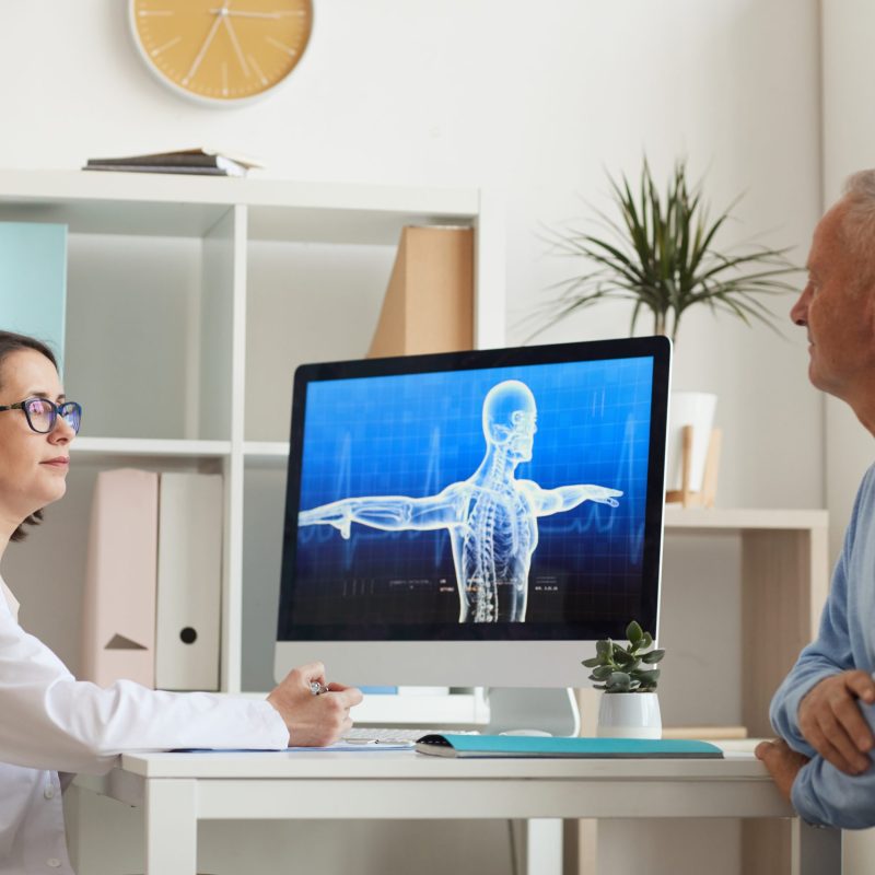 Side view portrait of female doctor consulting senior patient while sitting at desk in modern clinic interior, copy space