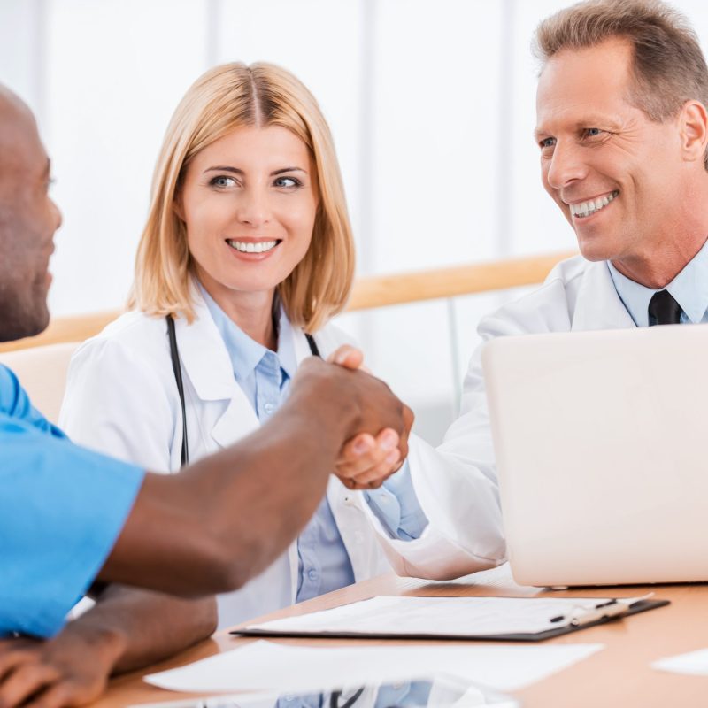 Doctors shaking hands. Two cheerful doctors shaking hands while sitting together with female doctor